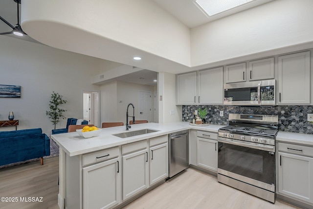 kitchen featuring sink, light hardwood / wood-style flooring, stainless steel appliances, decorative backsplash, and kitchen peninsula