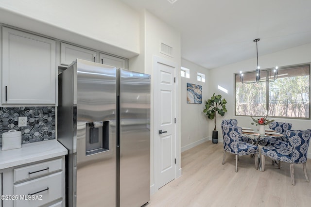 kitchen with pendant lighting, stainless steel fridge, an inviting chandelier, light stone counters, and light wood-type flooring