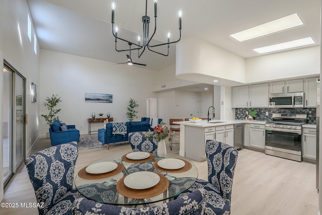 dining area with sink, a towering ceiling, light hardwood / wood-style flooring, and a skylight