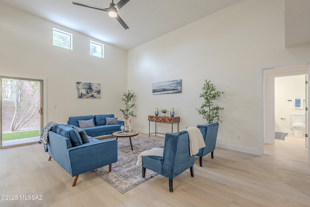 living room featuring ceiling fan, a high ceiling, and light wood-type flooring