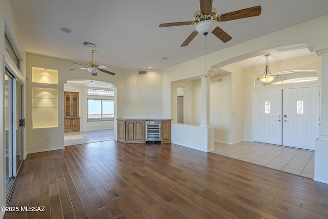 entryway featuring hardwood / wood-style floors, beverage cooler, ceiling fan, and ornate columns