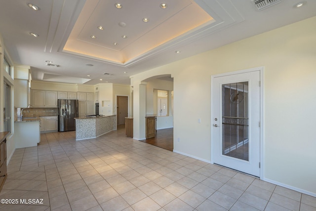 kitchen with stainless steel refrigerator with ice dispenser, light tile patterned flooring, sink, a raised ceiling, and decorative backsplash