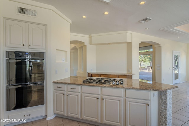 kitchen featuring light tile patterned floors, stainless steel gas stovetop, double oven, and white cabinets