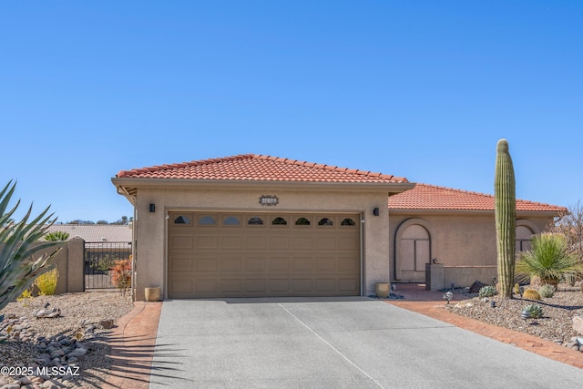 mediterranean / spanish home featuring a tile roof, stucco siding, an attached garage, fence, and driveway