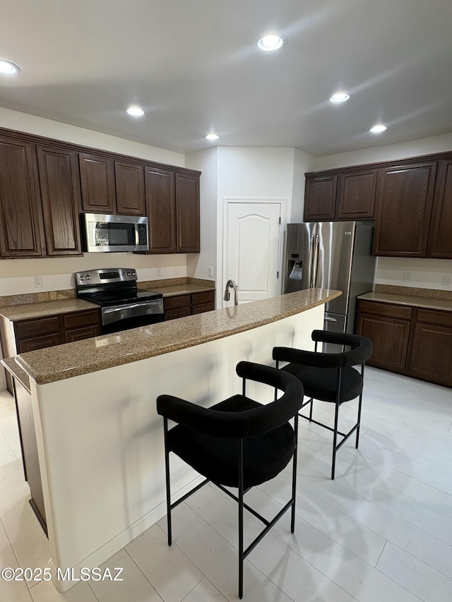 kitchen featuring sink, a kitchen bar, a kitchen island with sink, stainless steel appliances, and dark brown cabinets