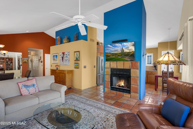 living room with ceiling fan, lofted ceiling, a tiled fireplace, and tile patterned flooring