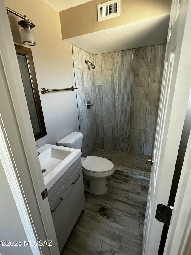 bathroom featuring tiled shower, vanity, and toilet