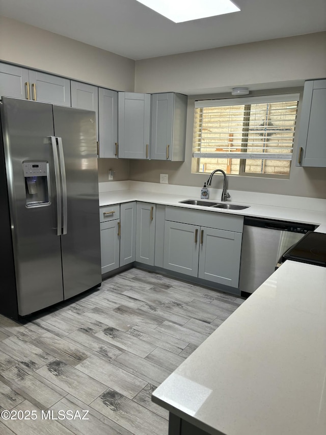 kitchen with stainless steel appliances, gray cabinets, sink, and light wood-type flooring