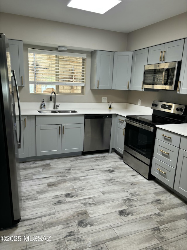 kitchen with gray cabinetry, sink, light wood-type flooring, and appliances with stainless steel finishes