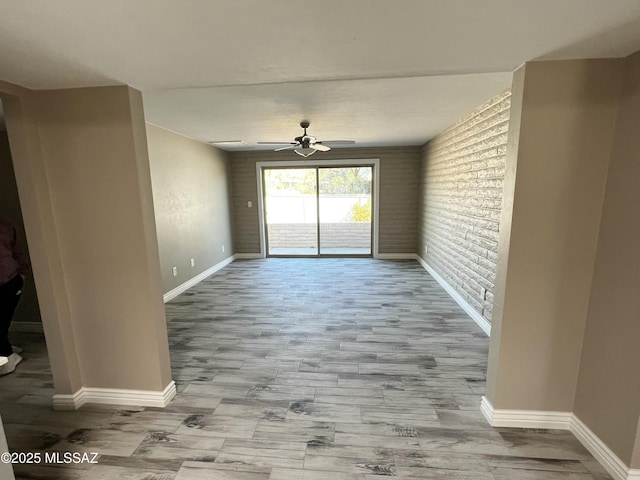 spare room with ceiling fan, brick wall, and light wood-type flooring