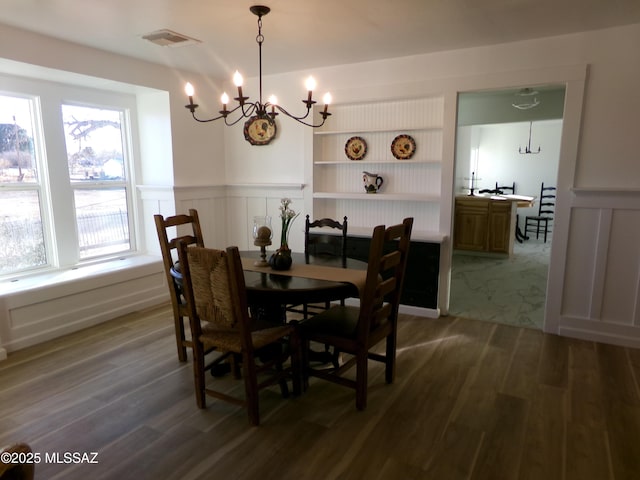 dining space with hardwood / wood-style flooring, built in shelves, and a notable chandelier