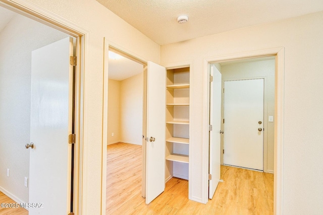 corridor featuring baseboards, light wood finished floors, and a textured ceiling