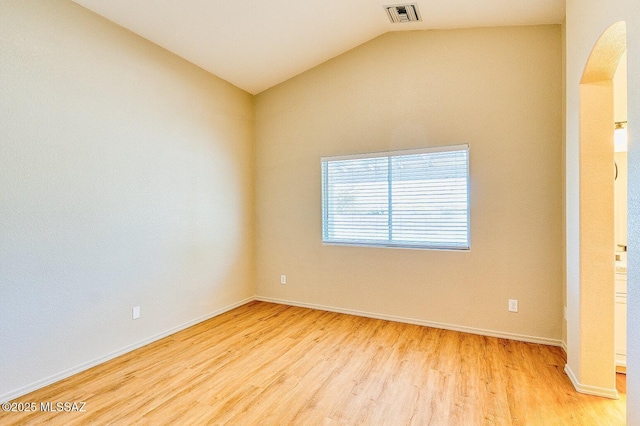 spare room with visible vents, lofted ceiling, arched walkways, light wood-style floors, and baseboards