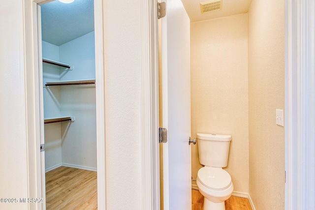 bathroom featuring visible vents, toilet, wood finished floors, baseboards, and a spacious closet