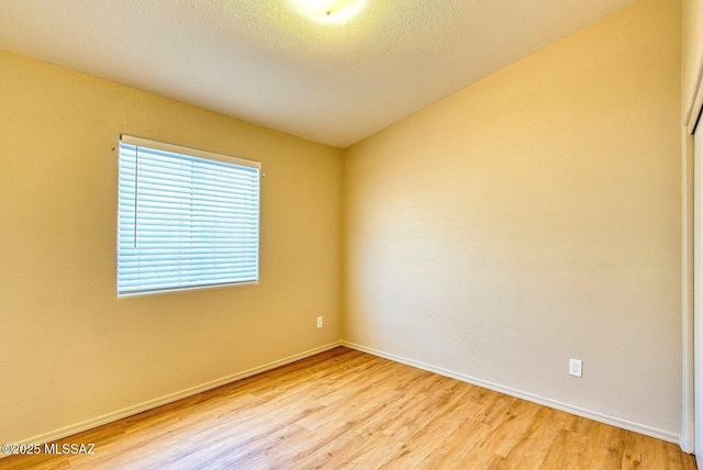 unfurnished room featuring light wood finished floors, a textured ceiling, and baseboards