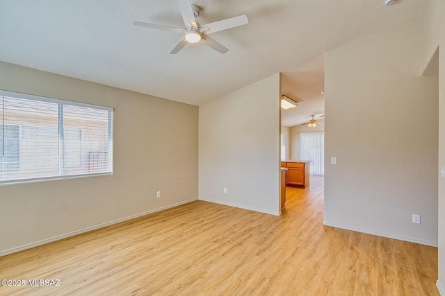 empty room featuring lofted ceiling, a healthy amount of sunlight, baseboards, and light wood finished floors