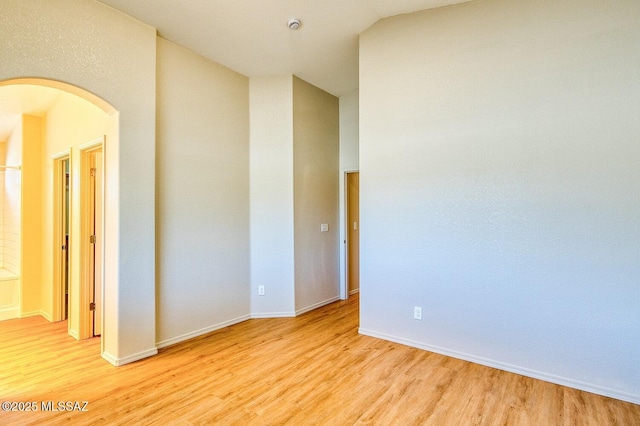 spare room with baseboards, arched walkways, and light wood-style flooring