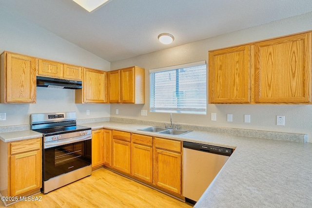 kitchen with light wood finished floors, under cabinet range hood, light countertops, appliances with stainless steel finishes, and a sink