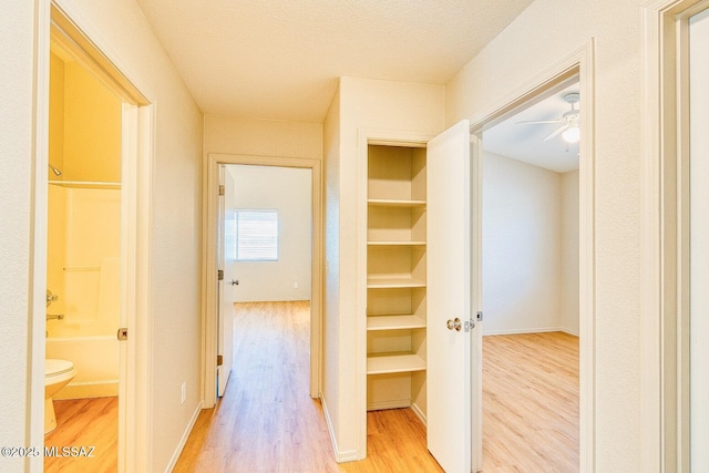 corridor with a textured ceiling, light wood-type flooring, and baseboards