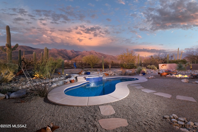 pool at dusk with an in ground hot tub, a mountain view, and a patio