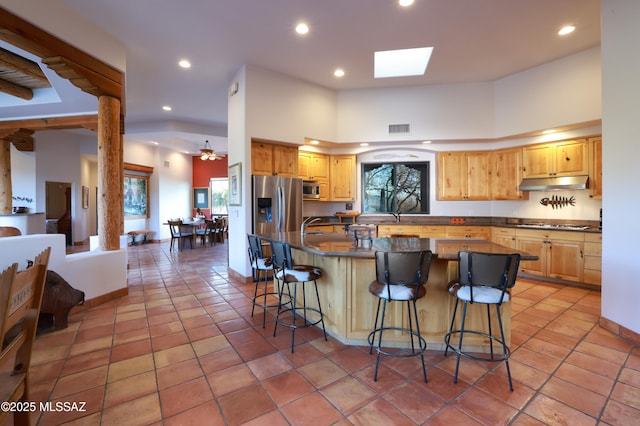 kitchen featuring appliances with stainless steel finishes, a towering ceiling, a center island, a kitchen bar, and light tile patterned flooring