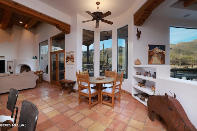 tiled dining area featuring beamed ceiling, ceiling fan, a fireplace, and a mountain view