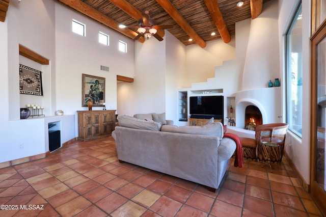 tiled living room featuring beam ceiling, wooden ceiling, a large fireplace, and ceiling fan