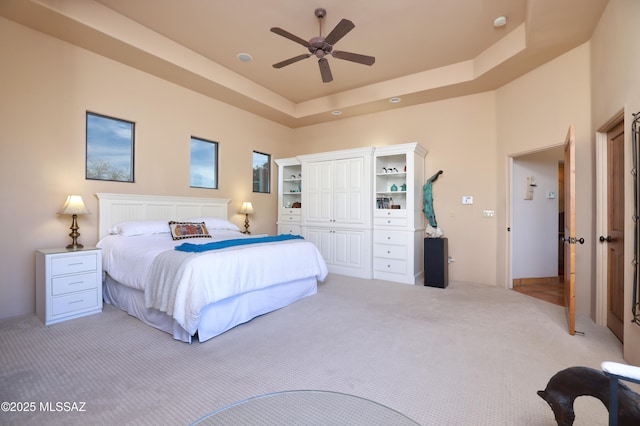 carpeted bedroom featuring a raised ceiling, ceiling fan, and a closet