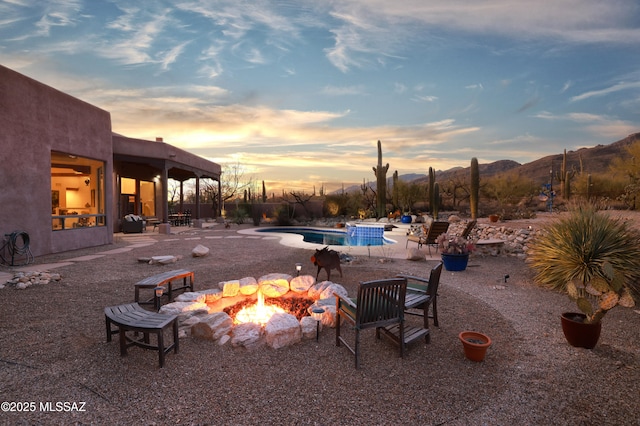 pool at dusk with a mountain view, a patio, and an outdoor fire pit