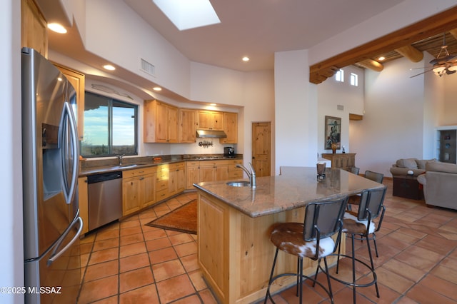 kitchen with light tile patterned flooring, a skylight, an island with sink, a towering ceiling, and stainless steel appliances