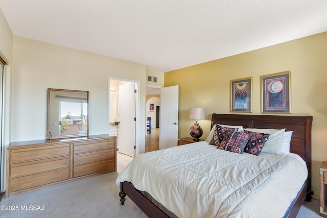 bedroom featuring light colored carpet, ensuite bathroom, and a textured ceiling