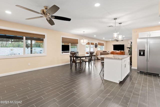 kitchen with light stone counters, stainless steel fridge with ice dispenser, hanging light fixtures, a kitchen island, and white cabinets