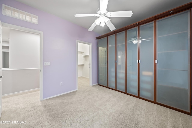 unfurnished bedroom with a walk in closet, light colored carpet, a closet, and ceiling fan