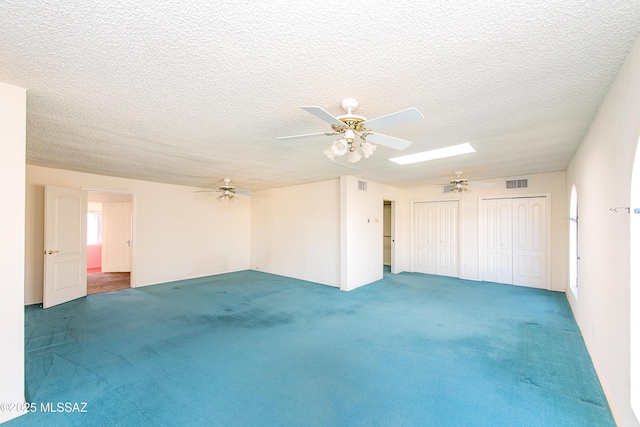 carpeted spare room with a textured ceiling, a skylight, and ceiling fan