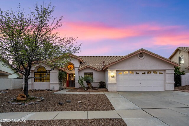 ranch-style house with an attached garage, fence, a tile roof, driveway, and stucco siding