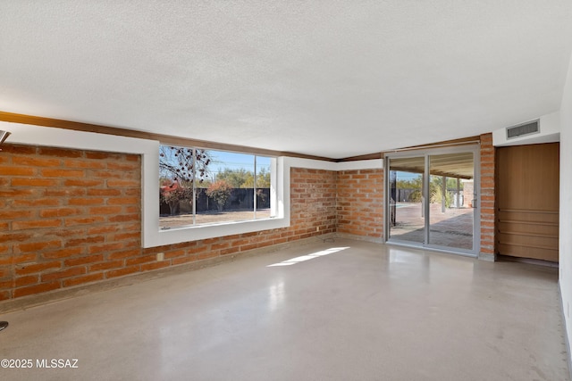 empty room with brick wall, a healthy amount of sunlight, and a textured ceiling