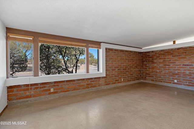 spare room with concrete flooring, brick wall, and a textured ceiling