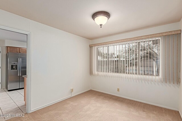 unfurnished room featuring light carpet, light tile patterned floors, and baseboards