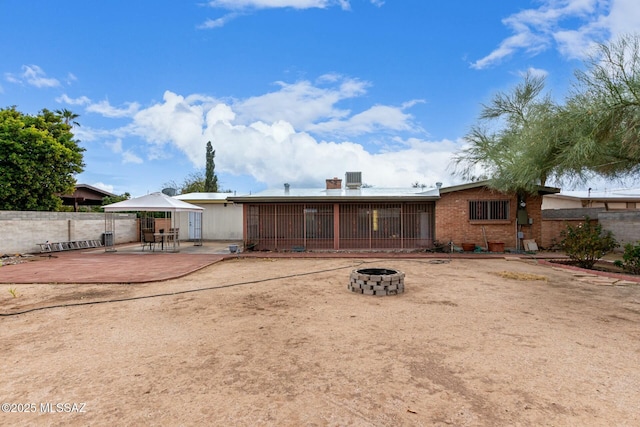 back of house featuring brick siding, a fire pit, a patio, and fence
