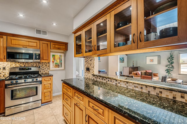 kitchen featuring dark stone countertops, tasteful backsplash, light tile patterned flooring, and appliances with stainless steel finishes