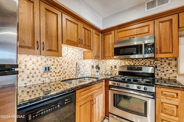 kitchen with backsplash, stainless steel appliances, sink, and dark stone counters