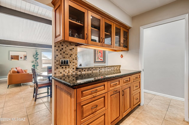 kitchen featuring tasteful backsplash, light tile patterned flooring, and dark stone countertops