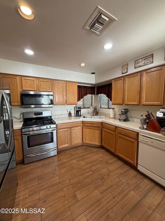 kitchen with appliances with stainless steel finishes, tile counters, sink, and hardwood / wood-style floors