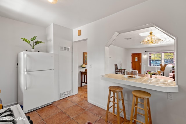 kitchen with light tile patterned floors, a breakfast bar, hanging light fixtures, white refrigerator, and kitchen peninsula