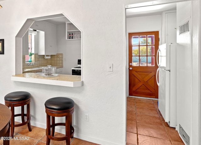 kitchen featuring light tile patterned flooring, white fridge, a breakfast bar area, and decorative backsplash