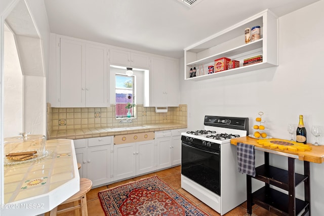 kitchen featuring sink, white cabinetry, backsplash, tile counters, and gas stove