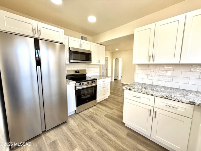 kitchen with white cabinetry, light wood-type flooring, light stone countertops, and appliances with stainless steel finishes