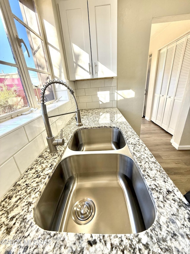 room details with hardwood / wood-style floors, white cabinetry, sink, backsplash, and light stone counters