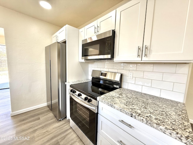 kitchen featuring appliances with stainless steel finishes, white cabinets, decorative backsplash, light hardwood / wood-style floors, and light stone countertops