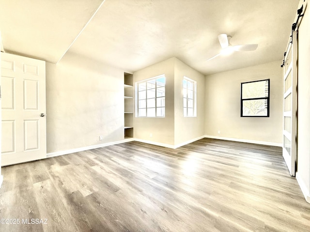 empty room with light hardwood / wood-style floors, a barn door, and ceiling fan